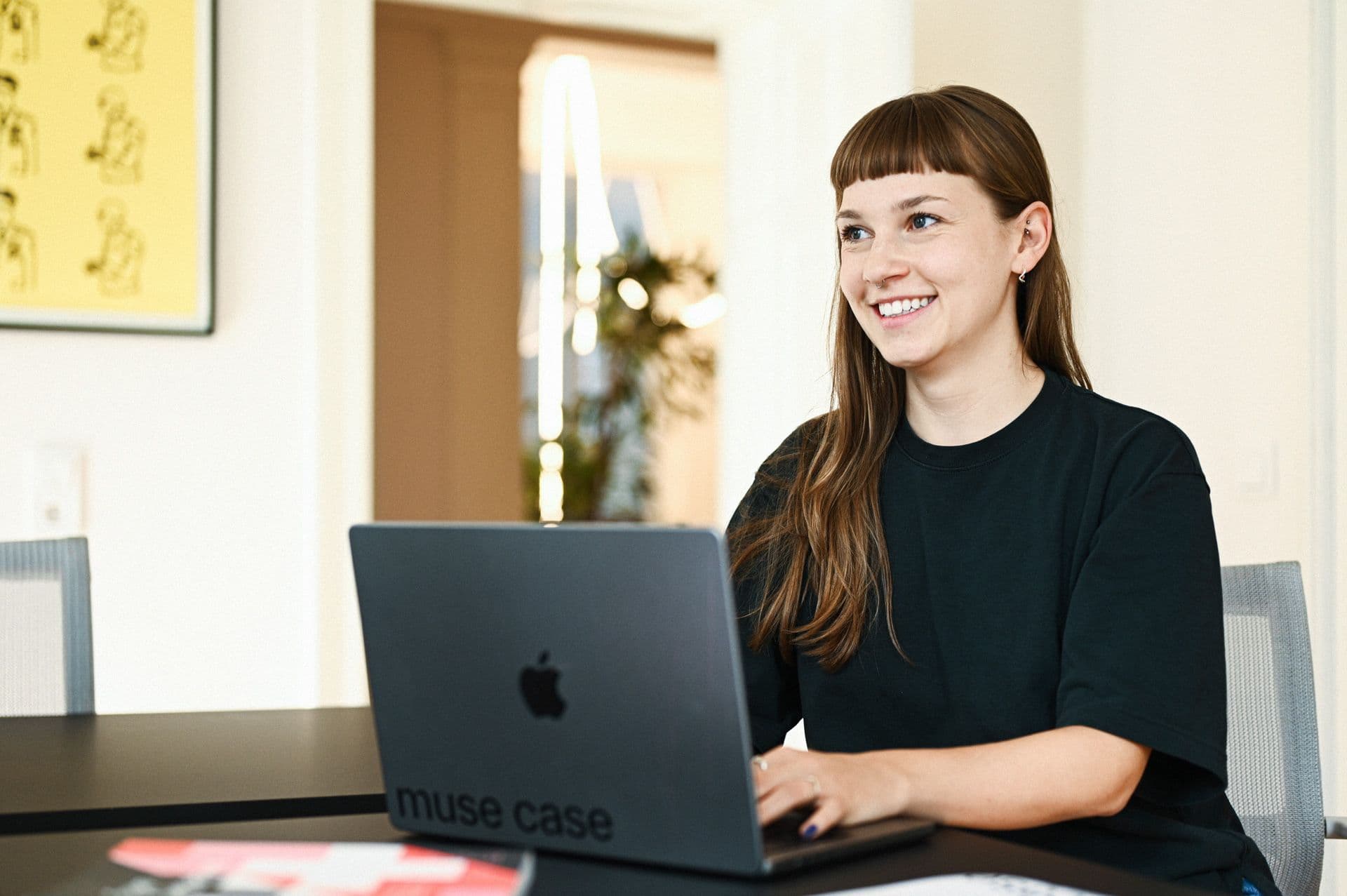 Lächelnde Frau arbeitet an einem muse case MacBook in einem modernen Büro.
